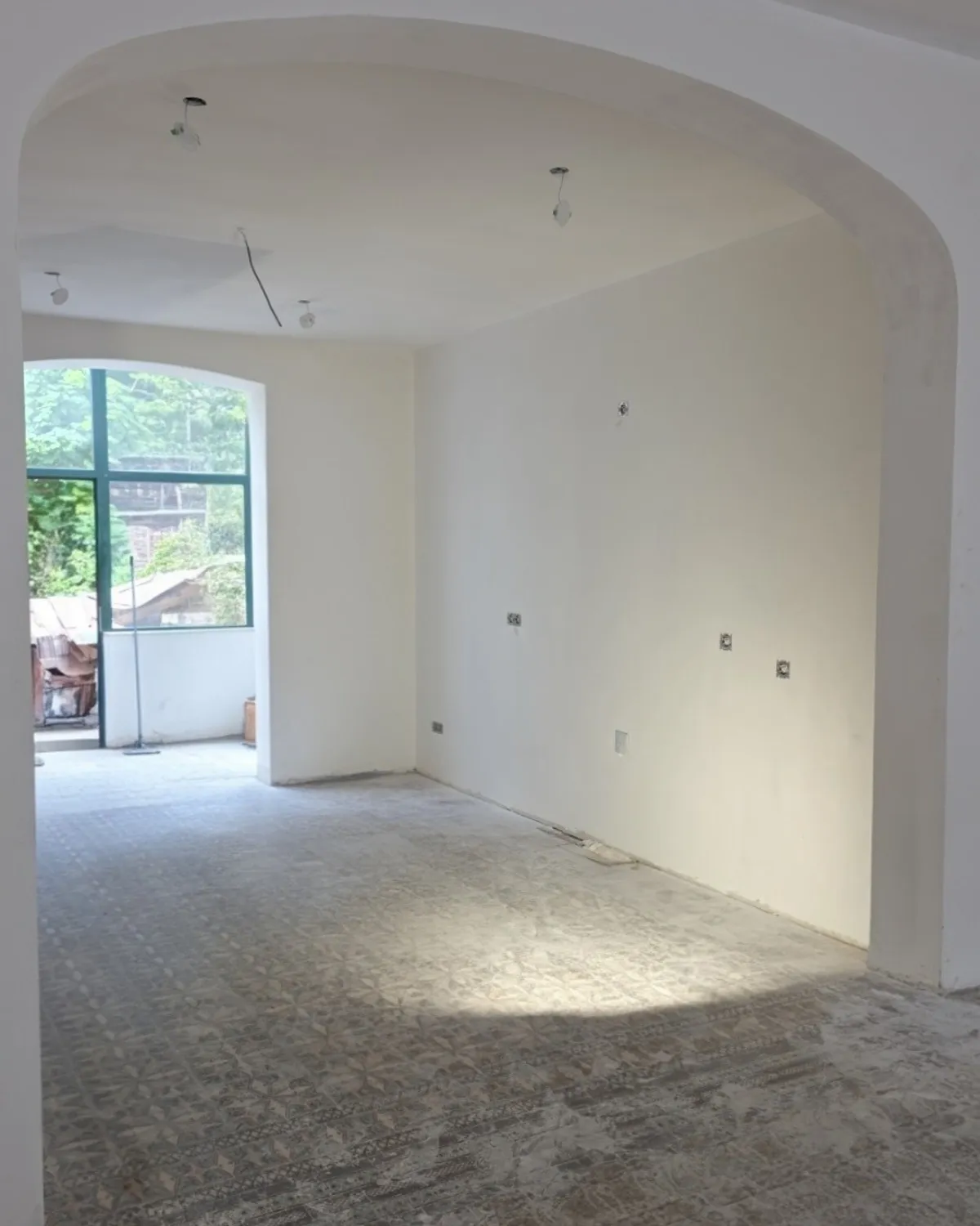 Séjour avant travaux : arche plâtrée, sol en carreaux ciment d'origine et baie cintrée donnant sur le jardin.