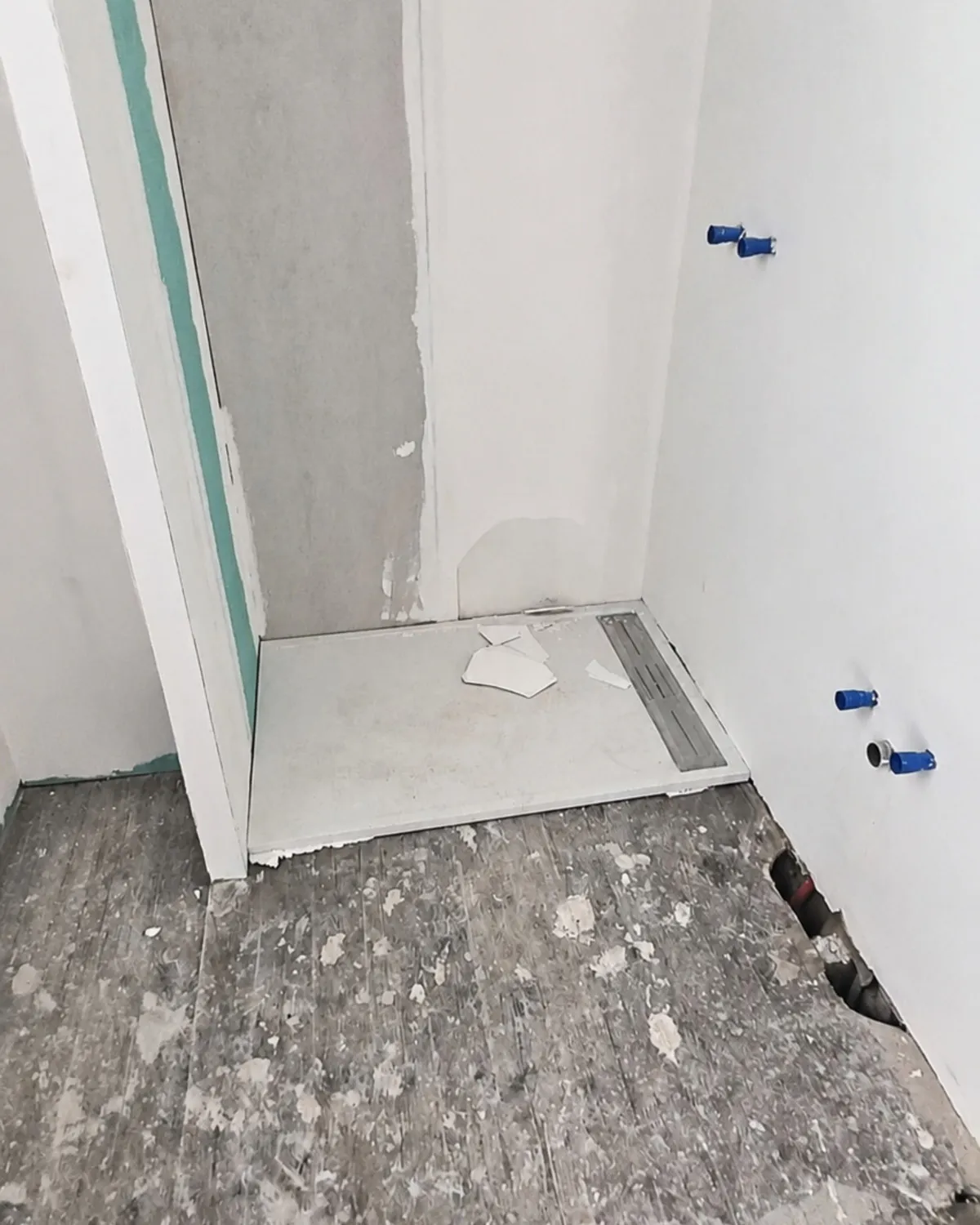 Salle de bain en chantier : receveur de douche posé, cloisons brutes et attentes de plomberie apparentes.